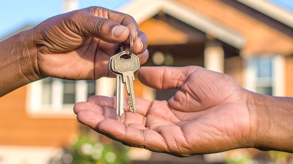 Hands passing keys one to another in front of a home